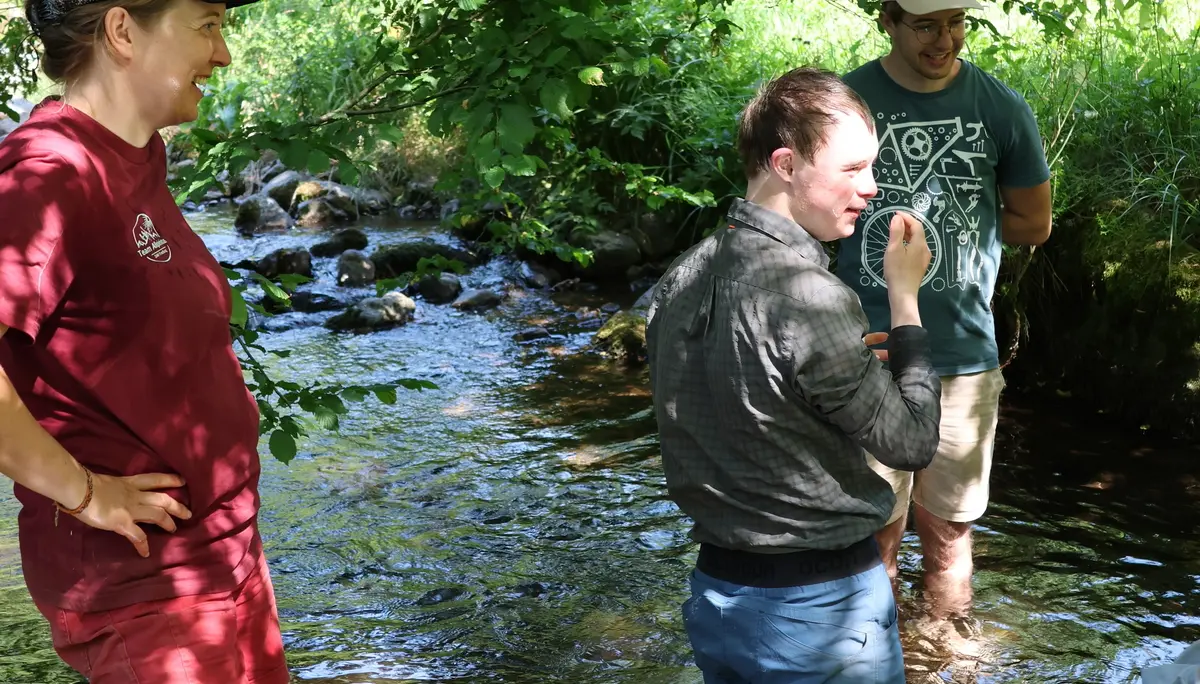 Drei Personen, zwei Betreuer*innen und ein Teilnehmer der Eselwanderung, stehen im Bach des Adamshofs und kühlen sich ab. | © DAV Sektion Freiburg-Breisgau / Kristin Schwarz