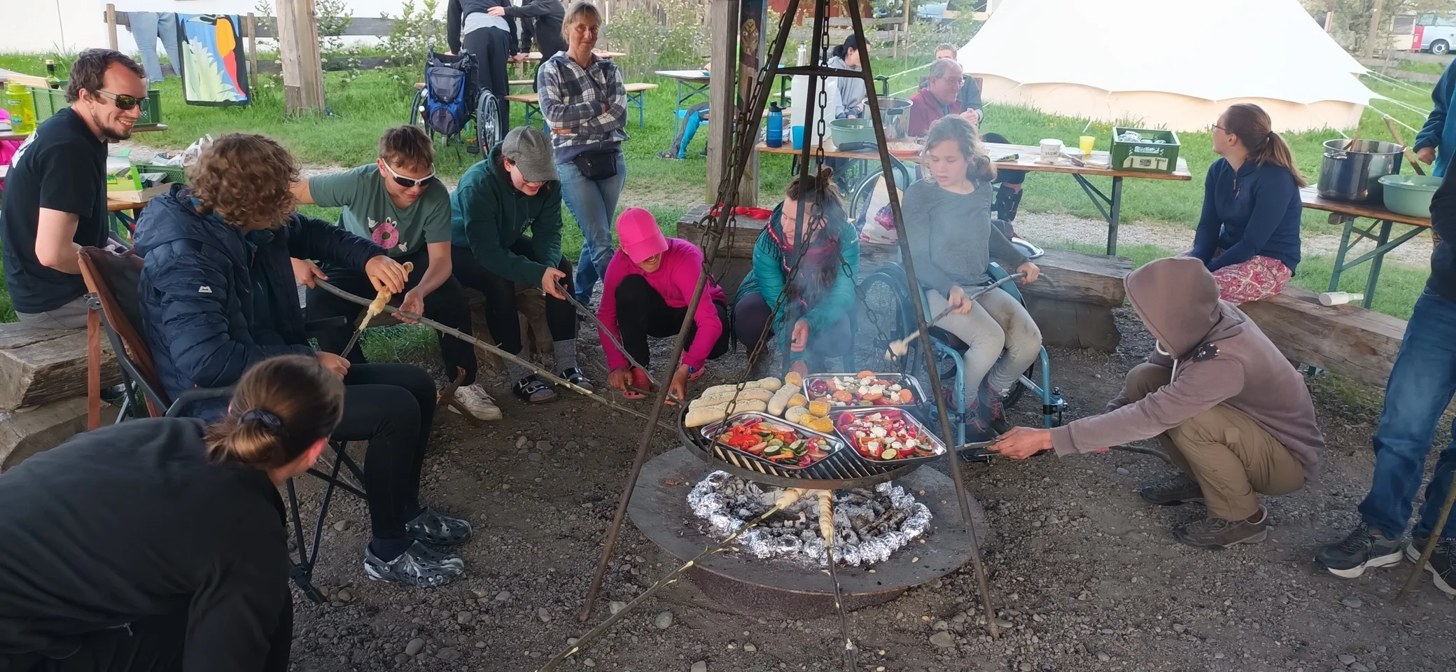 Kinder und Erwachsene sitzen um eine Feuerstelle und grillen Gemüse auf einem Rost und machen Stockbrot | © DAV/Freiburg-Breisgau/Josephine Kerzel/Inklusion/Ausfahrten