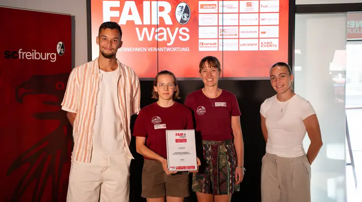 Stellvertretend für die Projektgruppe "Bunte Gipfel" nehmen die Allpinistas Miriam und Louisa (in der Mitte des Bildes) den FAIRways Förderpreis 2026 entgegen. Mit dabei: Mio Backhaus (rechts), Bundesliga-Team Männer des SC Freiburg, und Nora Scherer (links), Bundesliga-Team Frauen SC Freiburg | © SC Freiburg